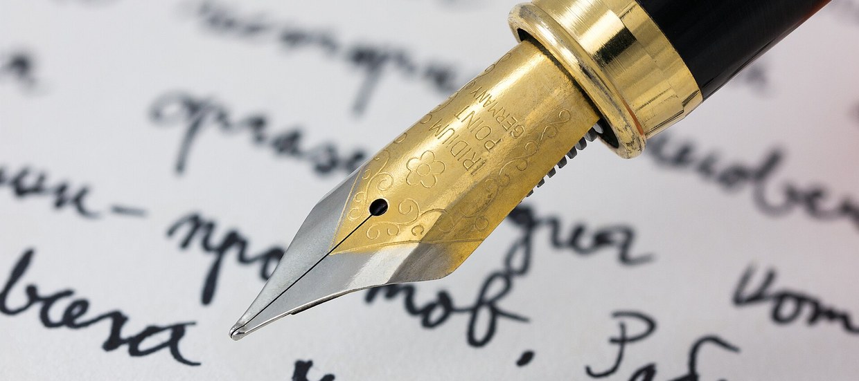 A hand writing in cursive on paper with a fountain pen