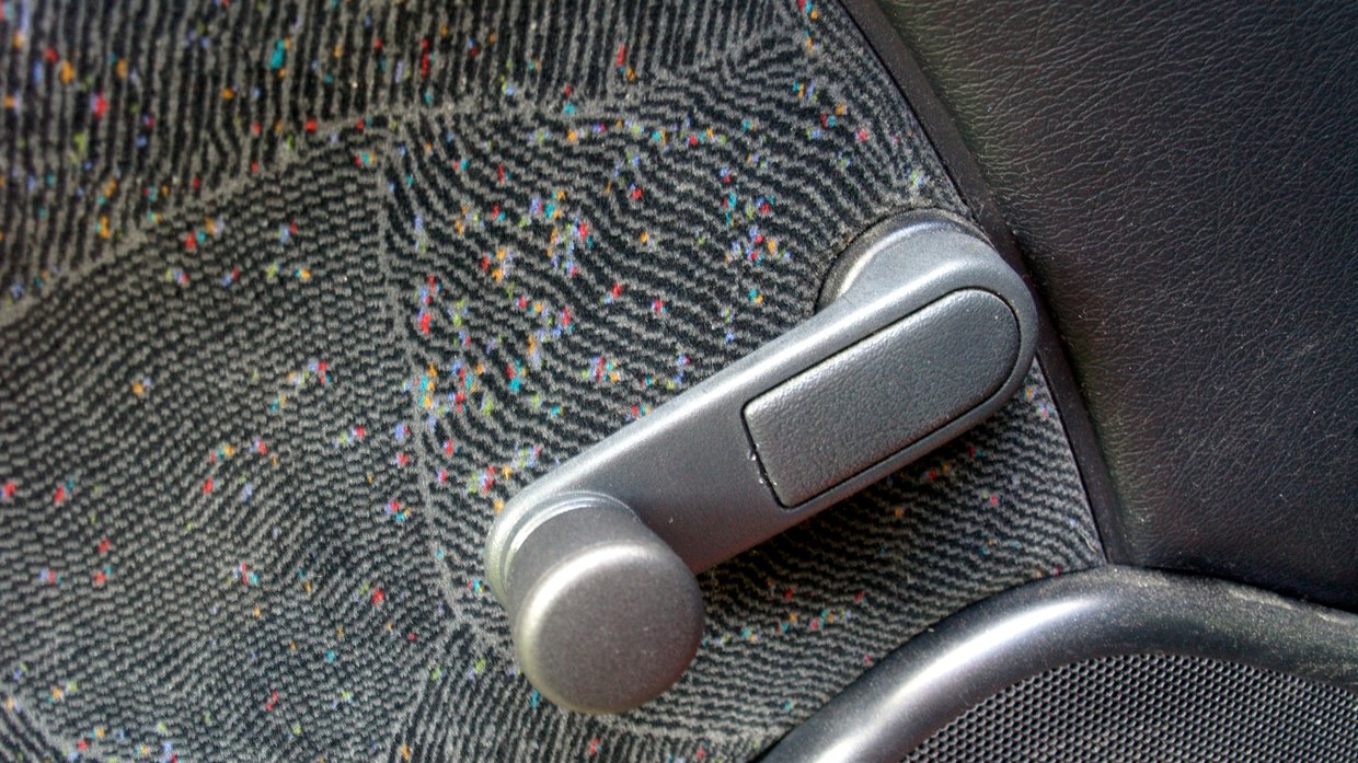 Close-up of a manual crank handle on a car door, set into grey speckled fabric trim